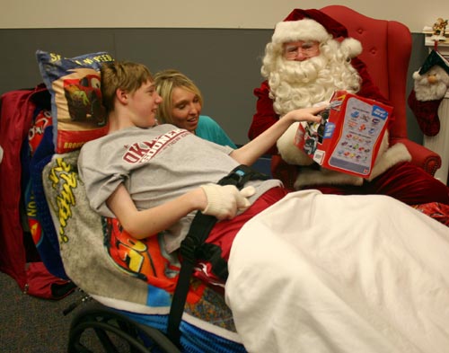 Fourteen- year-old Cale Smith, from Hinton, is all smiles as Santa Claus presents him with one of several gifts provided by the Oklahoma Municipal Contractors Association during their annual Christmas party for the inpatients of the J. D. McCarty Center in Norman. Looking on is Smith's direct care specialist Karri Hokett.