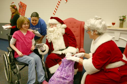 Santa and Mrs. Claus unload a bag full of goodies for 15-year old Jacee Palmer from Muskogee during the Oklahoma Municipal Contractors Association annual Christmas party for the inpatients of the J. D. Mccarty Center. Assisting Palmer with her gifts is McCarty Center direct care specialist Kerri Onken.