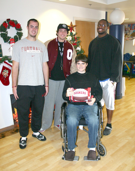 J. D. McCarty Center patient Jared Goss of Vinita, Oklahoma, proudly shows off his newly autographed football that he received during a surprise visit from members of the University of Oklahoma football team. The visit was made possible by Katie Slagel (l) and Callyn Honse who are volunteers with the Oklahoma chapter of the Make-A-Wish Foundation.  Goss' visitors were (l-r) Landry Jones, Matt Mooreland and Gerald McCoy