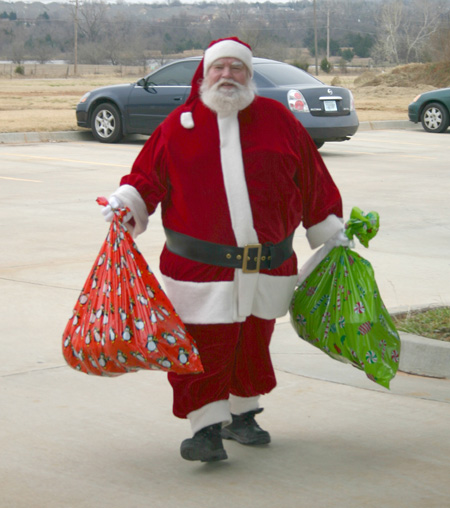 Santa Claus, aka OU Hourly Employee Council member Ed Fontane, brings bags of bicycle helmets, training wheels, knee pads and elbow pads to the J. D. McCarty Center as a part of the council's donation of 20 bicycles and tricycles. The McCarty Center children were the beneficiaries of the council's annual Christmas project. The group raised $1,000 for the purchase of the bikes and equipment.