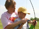 Image of a Staff Member Teaching a Boy with a Bow and Arrow